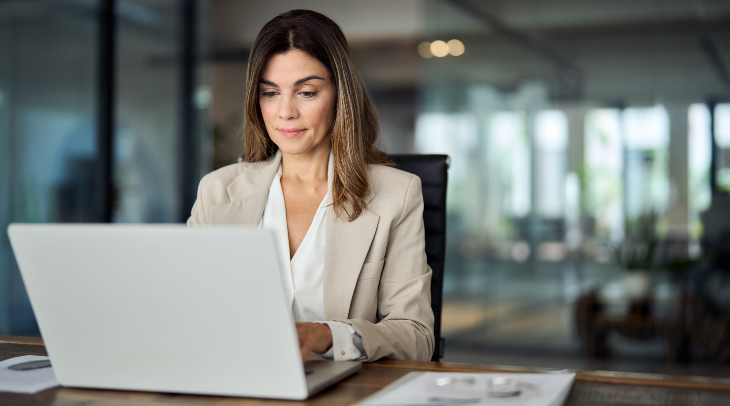 Businesswoman in suit sat at a desk in an office using laptop to prepare with SpeechLive Legal Direct