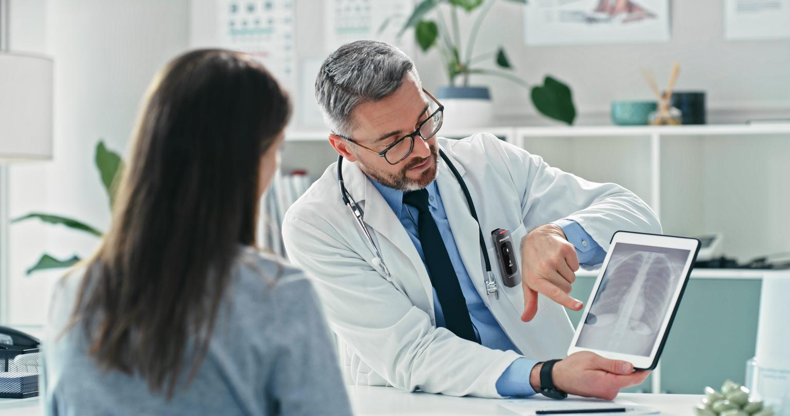 Male doctor talking to female patient while recording with Philips SpeechMike Ambient