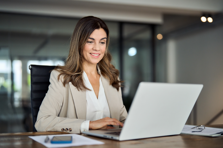 Businesswoman in suit sat at a desk in an office using laptop to prepare with SpeechLive Legal Direct